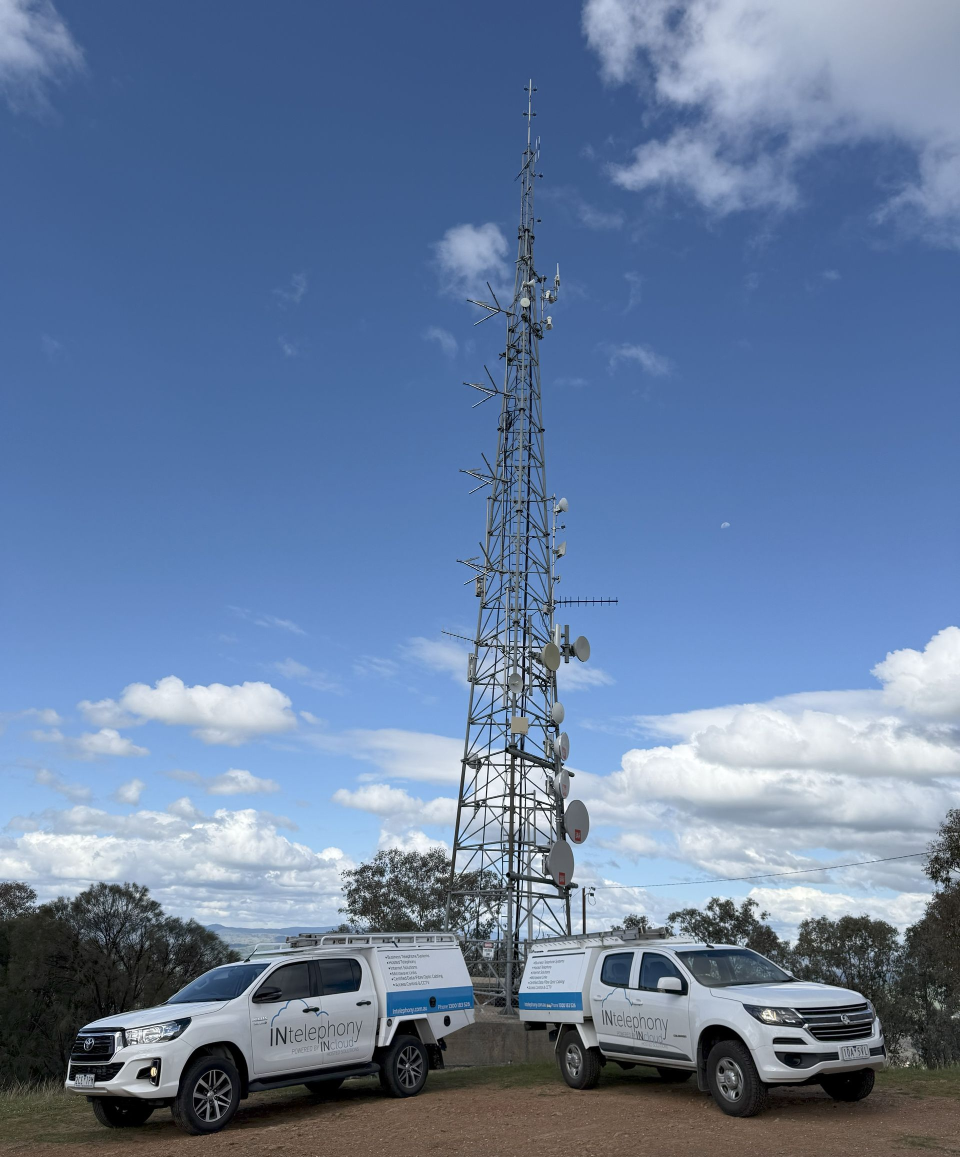 Two white trucks with trailers in front of a tall communication tower against a blue sky with clouds — INtelephony In Albury, NSW