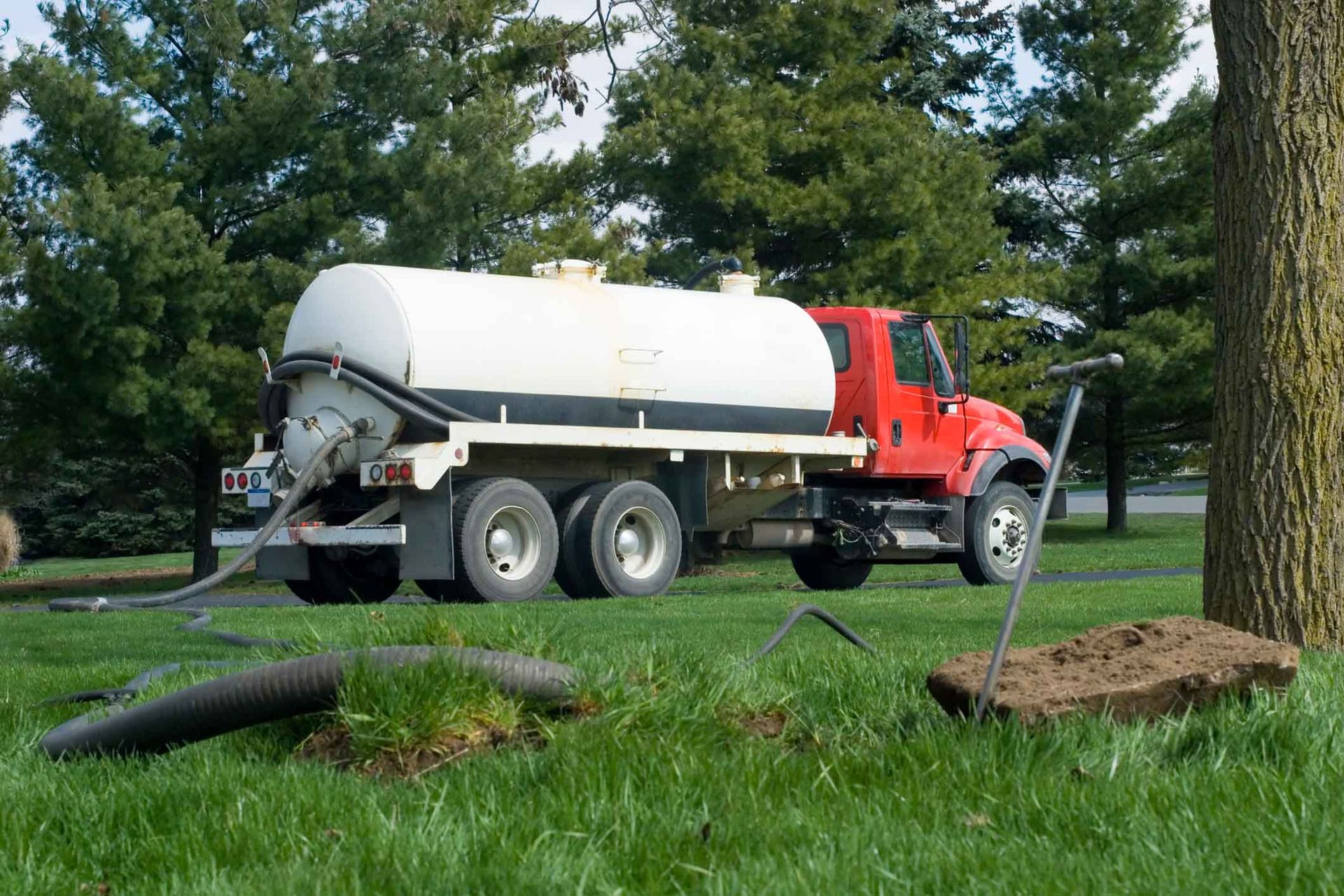 A red and white septic tank truck is parked in a grassy field.
