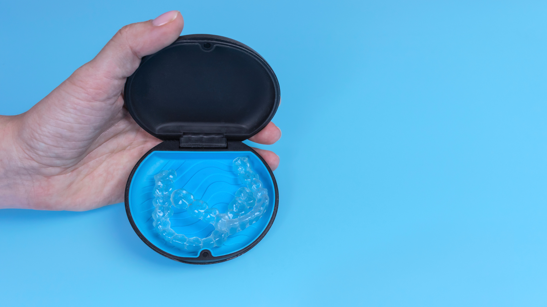 A person is holding a clear retainer in a case on a blue background.