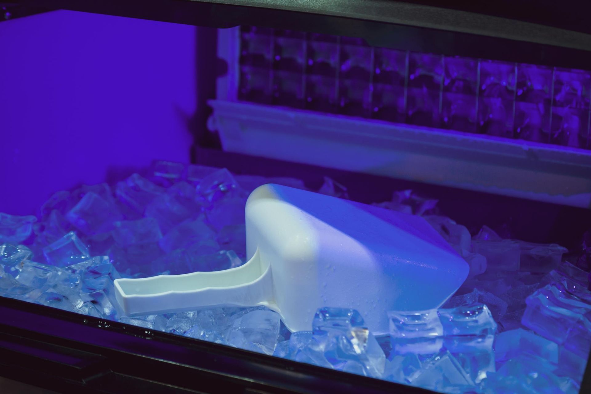 A White Ice Scoop Resting in a Bin Filled With Ice Cubes Under Blue-tinted Lighting — Cool Blue Ice & Water in Tamworth, NSW