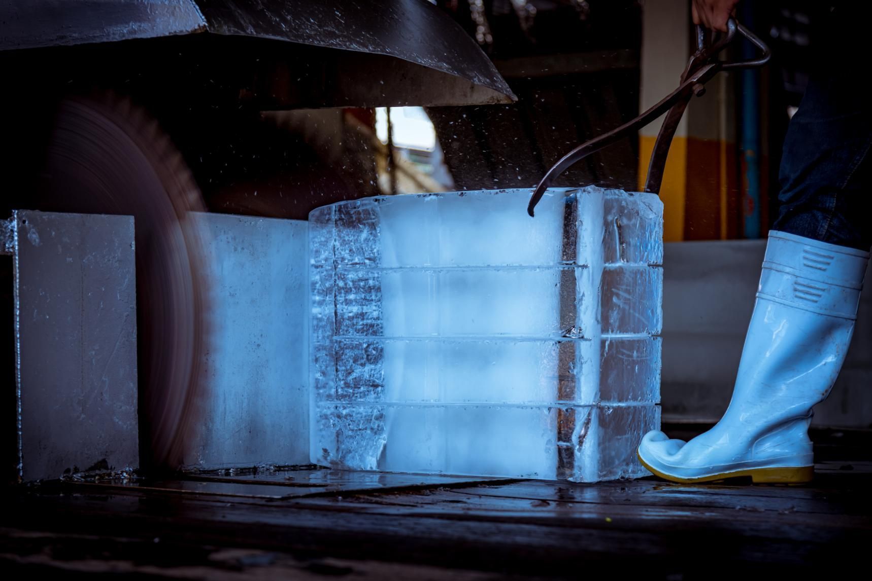 A Person in White Rubber Boots Uses a Large Saw to Cut a Massive Block of Ice — Cool Blue Ice & Water in Taminda, NSW