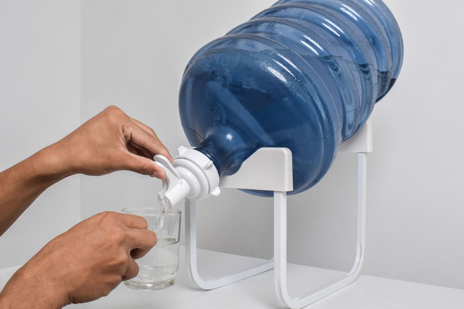 A Person Pouring Water From a Blue Plastic Jug Sitting on a White Metal Stand — Cool Blue Ice & Water in Taminda, NSW