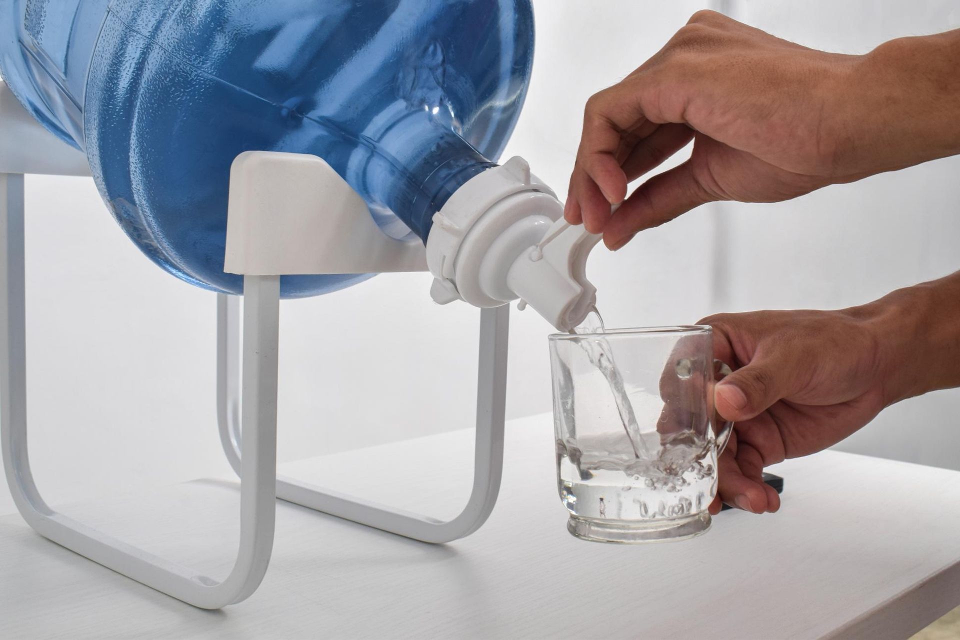A Person Pouring Water From a Blue Plastic Jug on a White Stand Into a Clear Glass — Cool Blue Ice & Water in Cobar, NSW