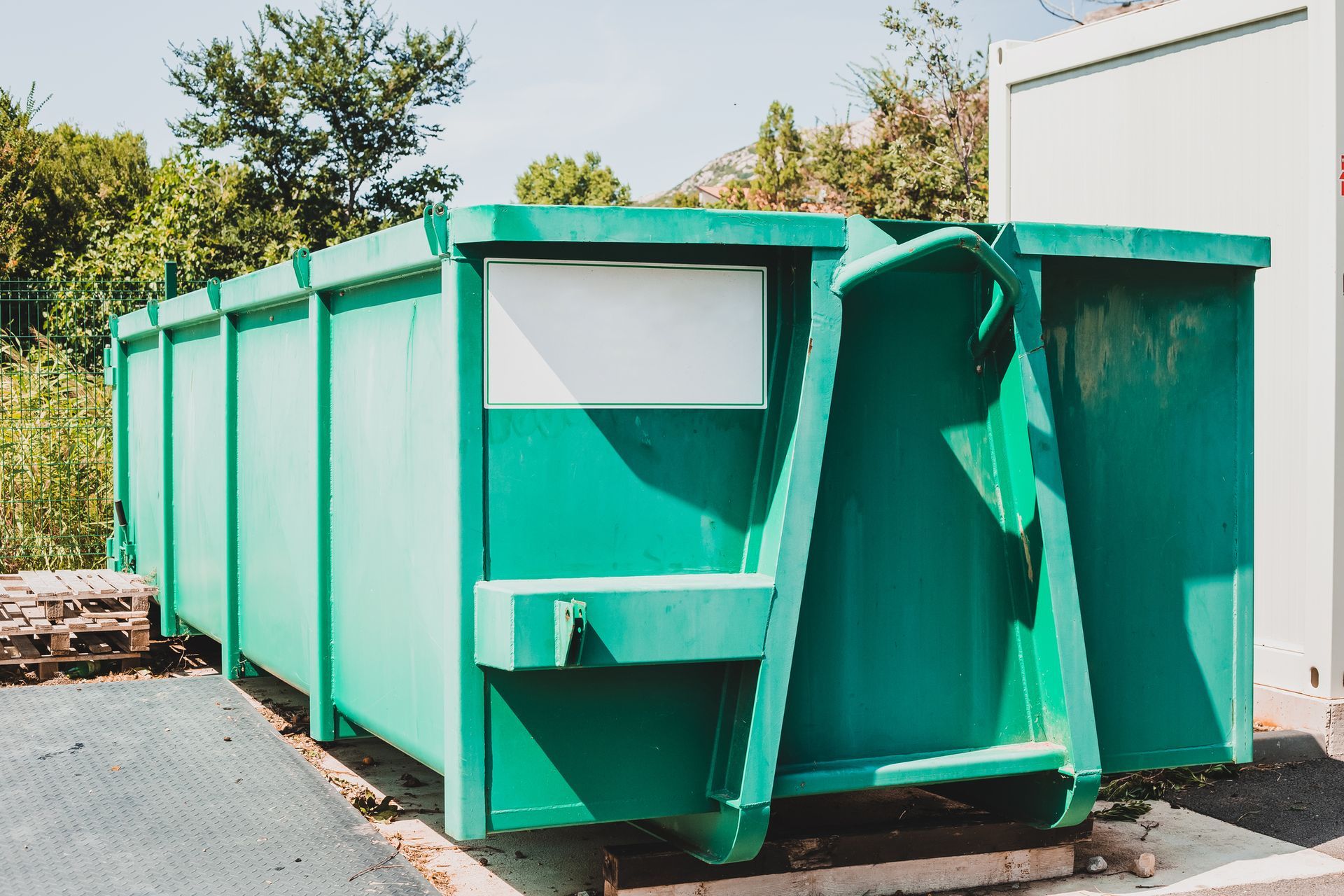 A green dumpster with a broom in front of it.