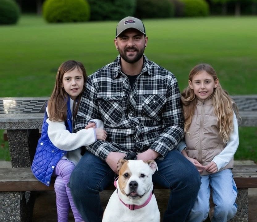 Man sitting on a bench with two children and a white dog in a park, green grass behind them
