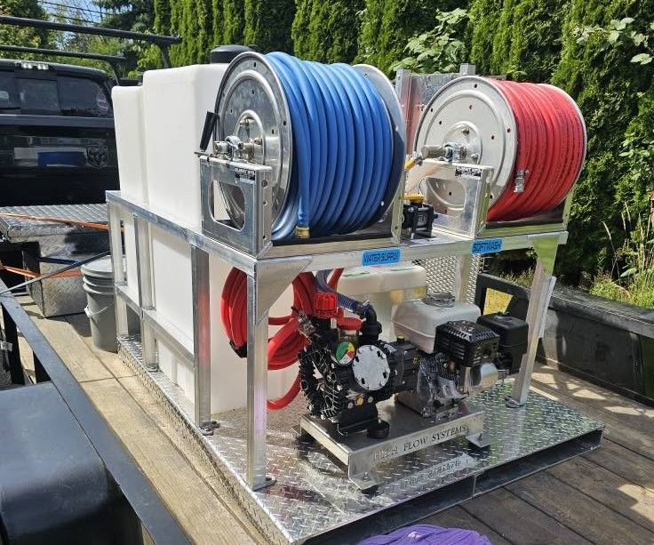 Two hose reels, blue and red, mounted on a metal trailer with pumps and equipment outdoors.