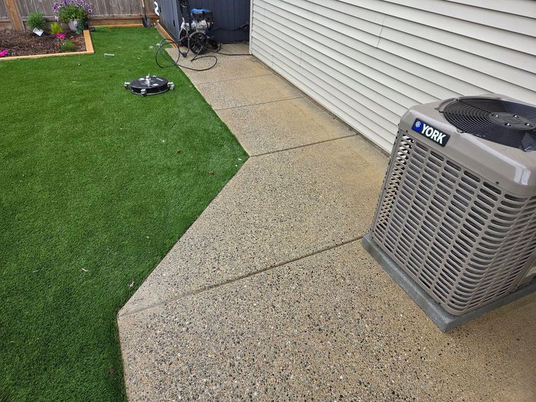 Backyard patio beside green lawn, with an outdoor AC unit near a house wall.