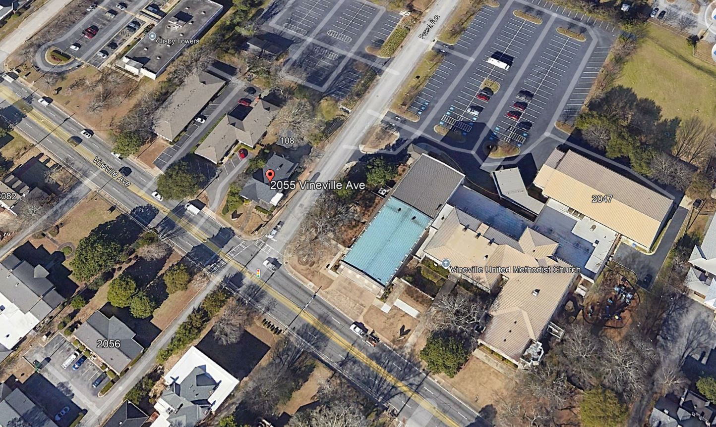 Aerial view of a campus-like complex with beige buildings, parking lots, and tree-lined roads.