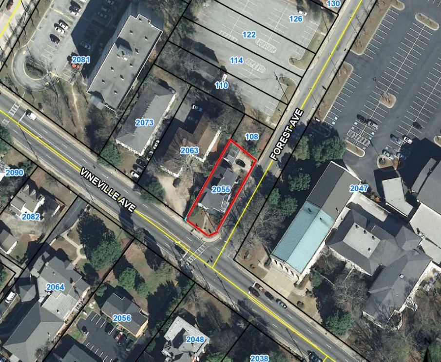Aerial view of a small property outlined in red beside a street and parking lot.