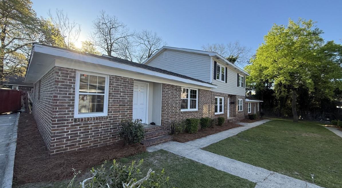 Brick house exterior with white trim, front door, walkway, and green lawn under sunny sky