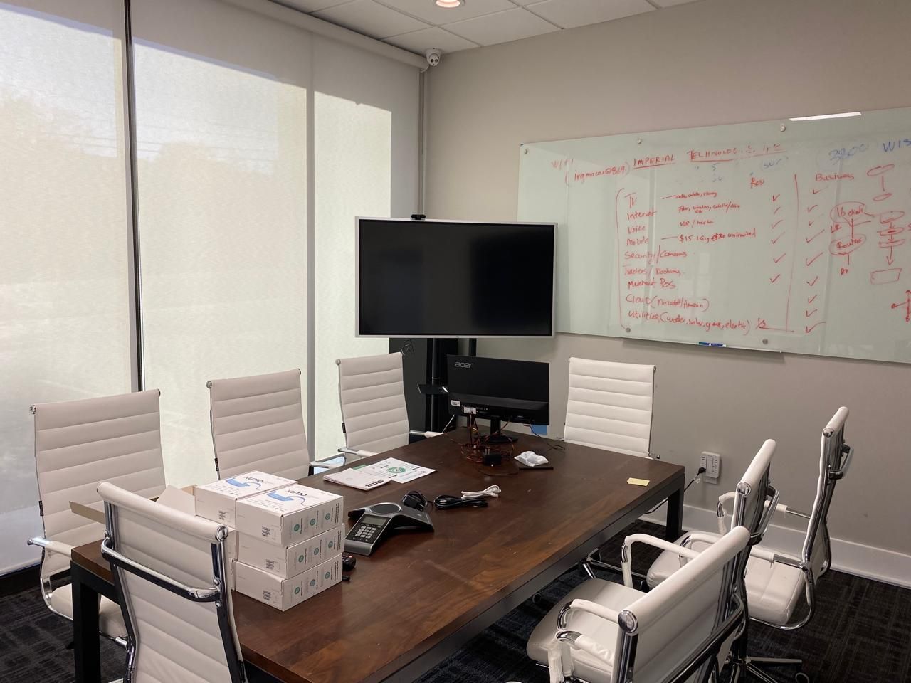 Conference room with a large table, chairs, TV, and whiteboard in a bright office.