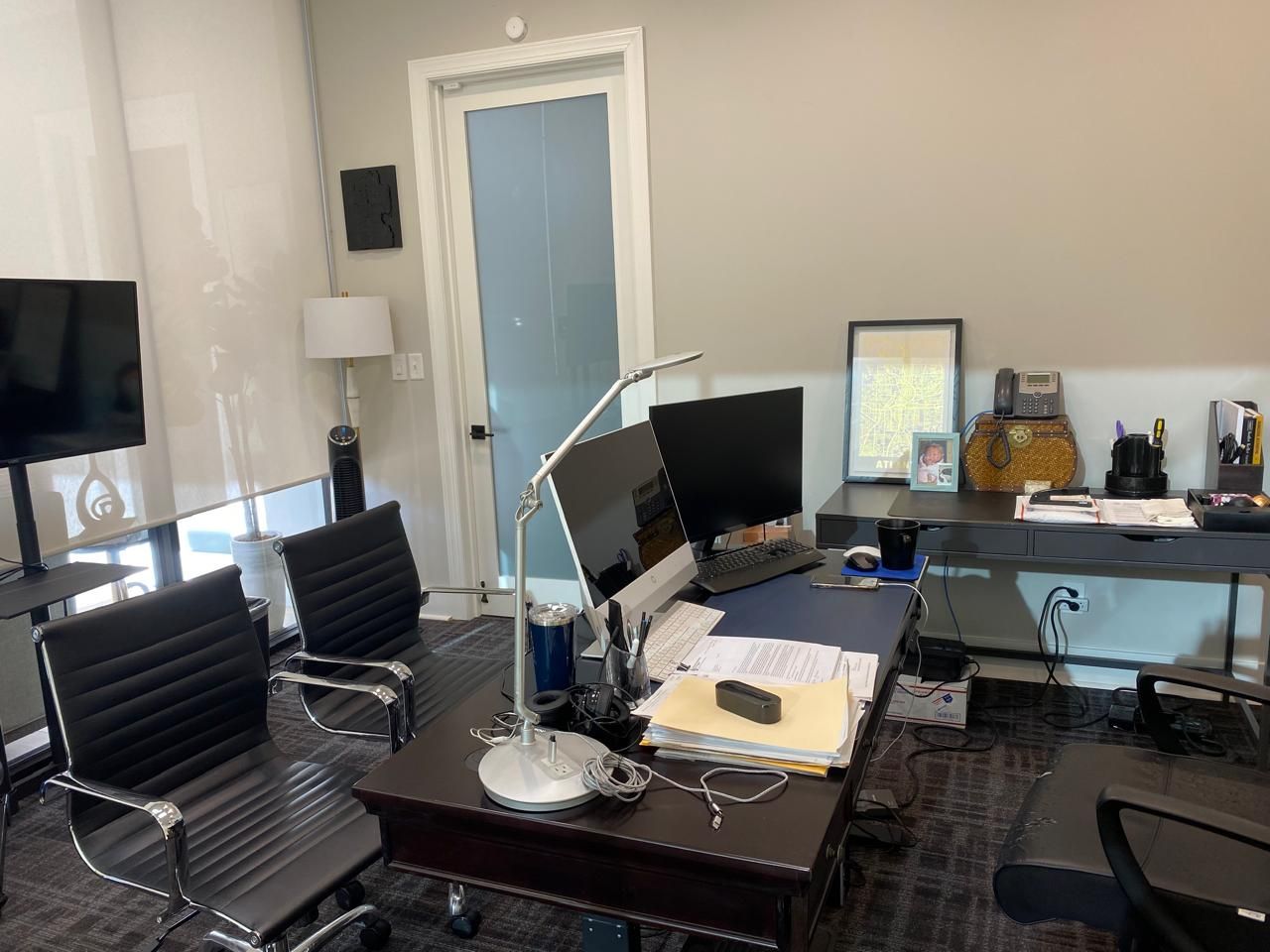 Modern office with black chairs, glass desk, monitor, floor lamp, and a blue door in the background