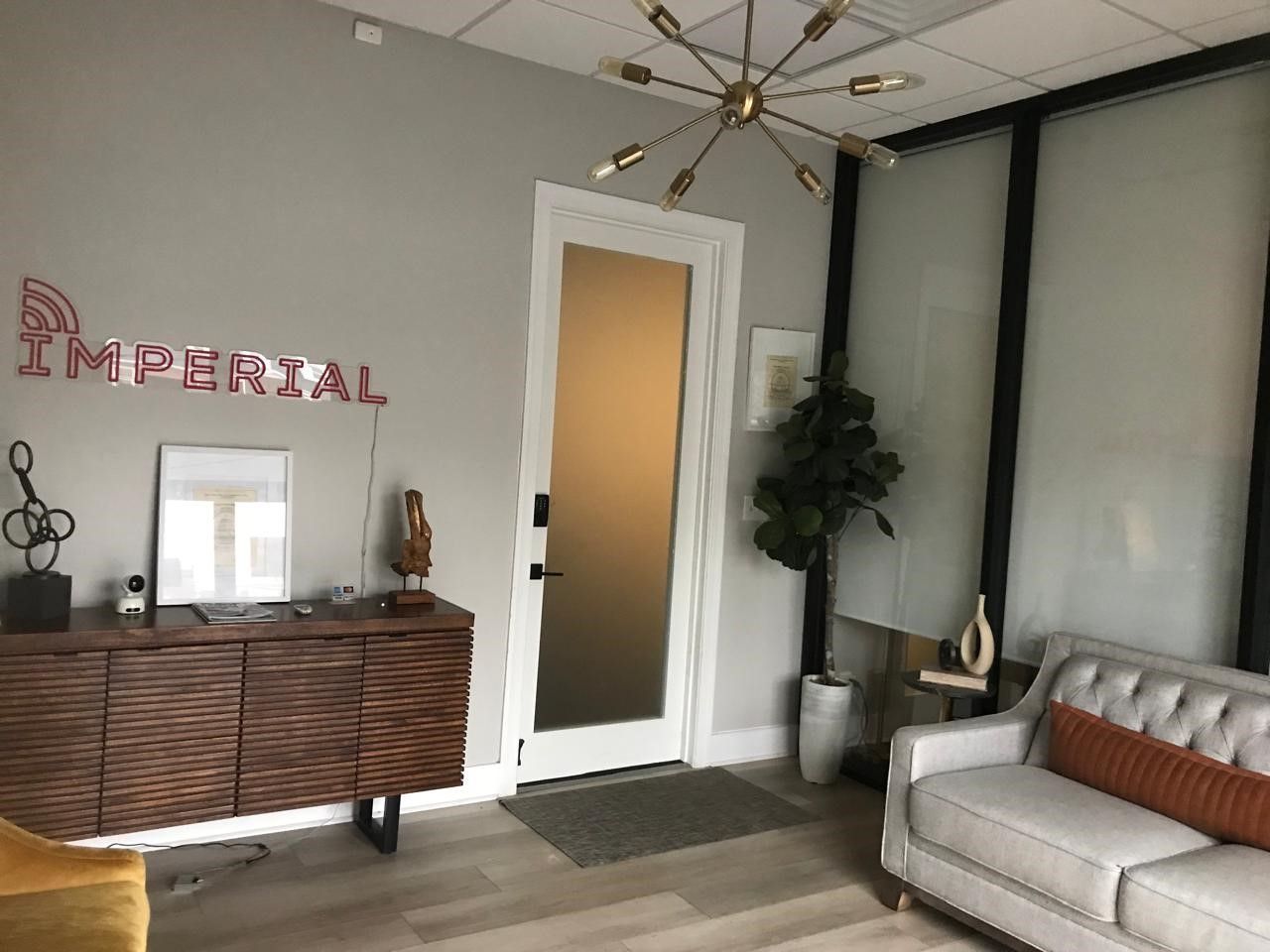 Modern waiting room with wicker cabinet, gray sofa, plant, and frosted glass wall panels