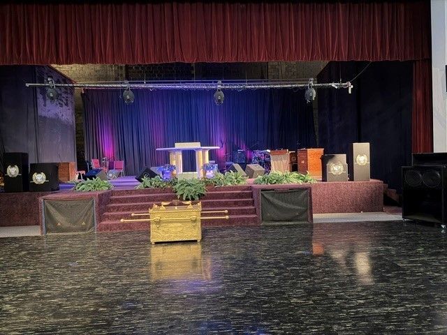 Church stage decorated with purple lights, greenery, and a central podium in an empty hall