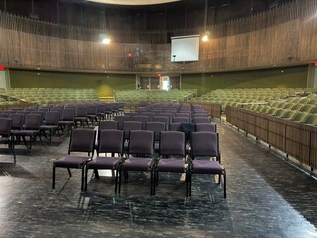Empty auditorium with rows of purple chairs facing a stage and green seating in the background