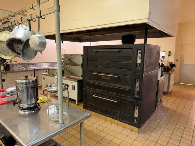 Industrial kitchen with large black oven and stainless steel prep table with hanging pots and pans