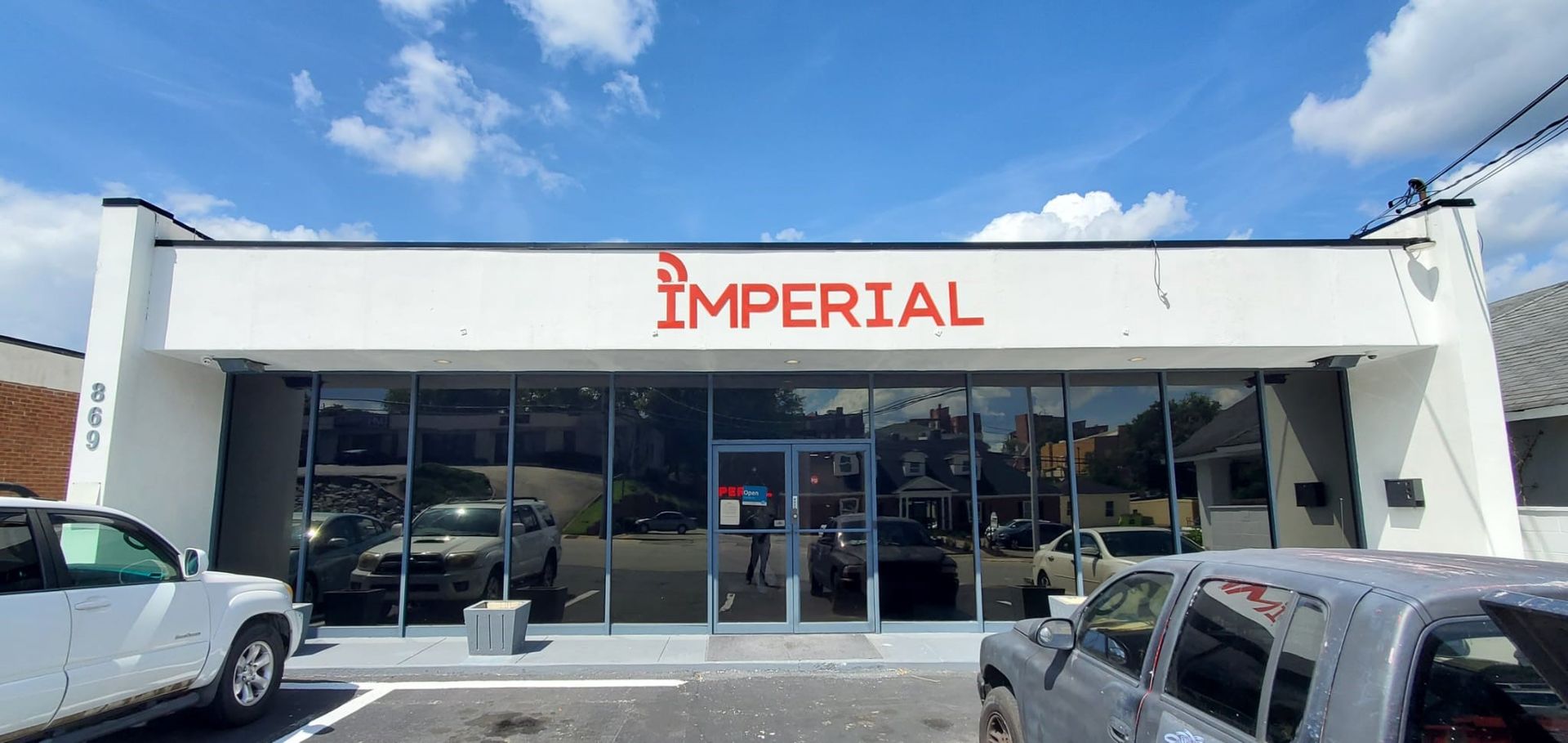 Imperial storefront with glass windows, white facade, and parked cars in front