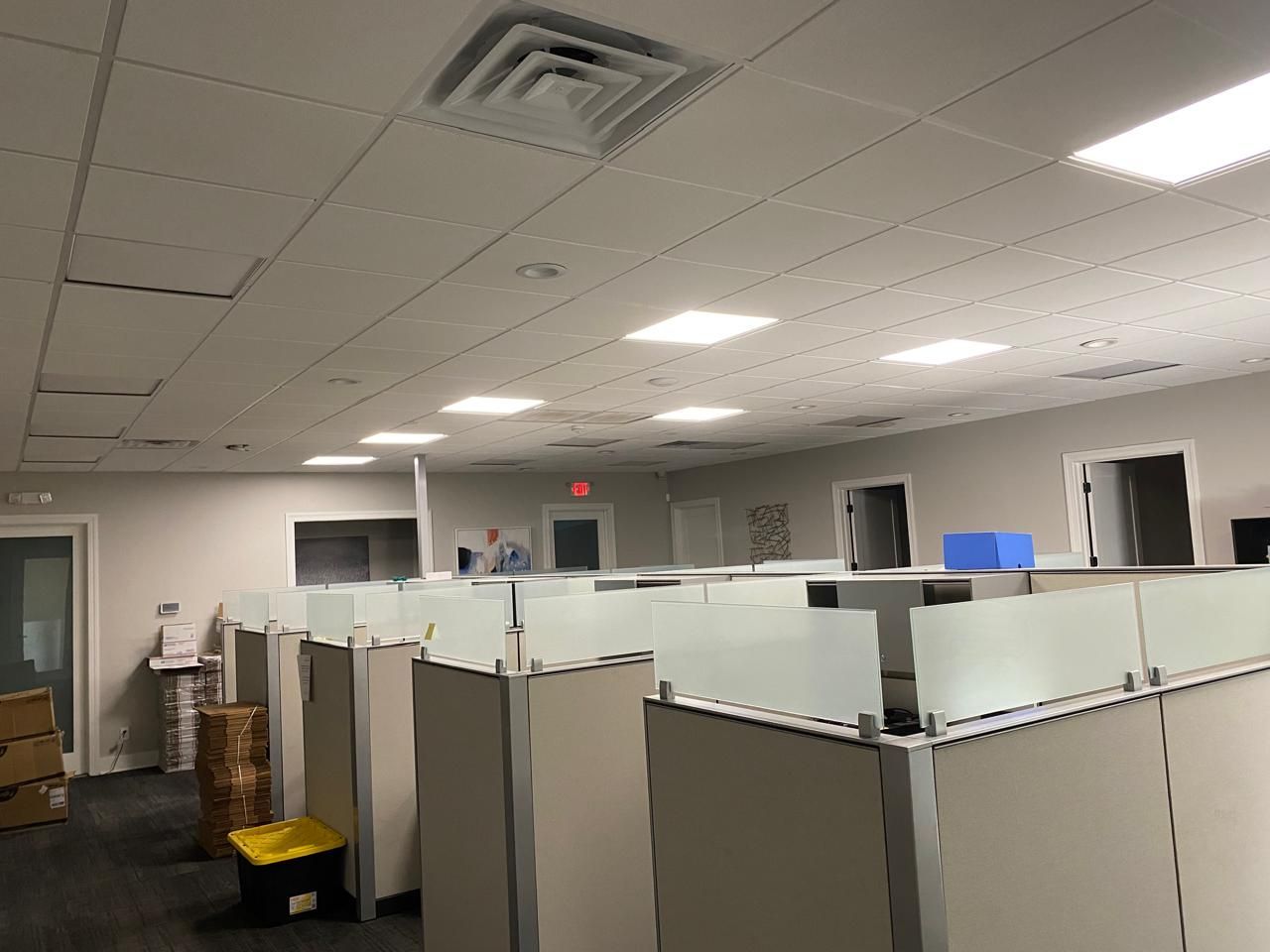 Empty office cubicle area with gray partitions, white ceiling tiles, and fluorescent lights