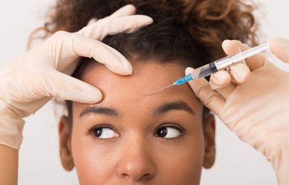 A woman is getting a botox injection in her forehead.