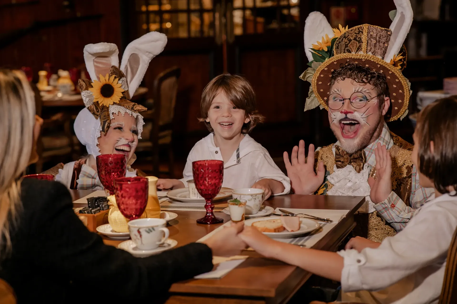 Crianças fantasiadas rindo em uma mesa com bebidas durante uma festa.