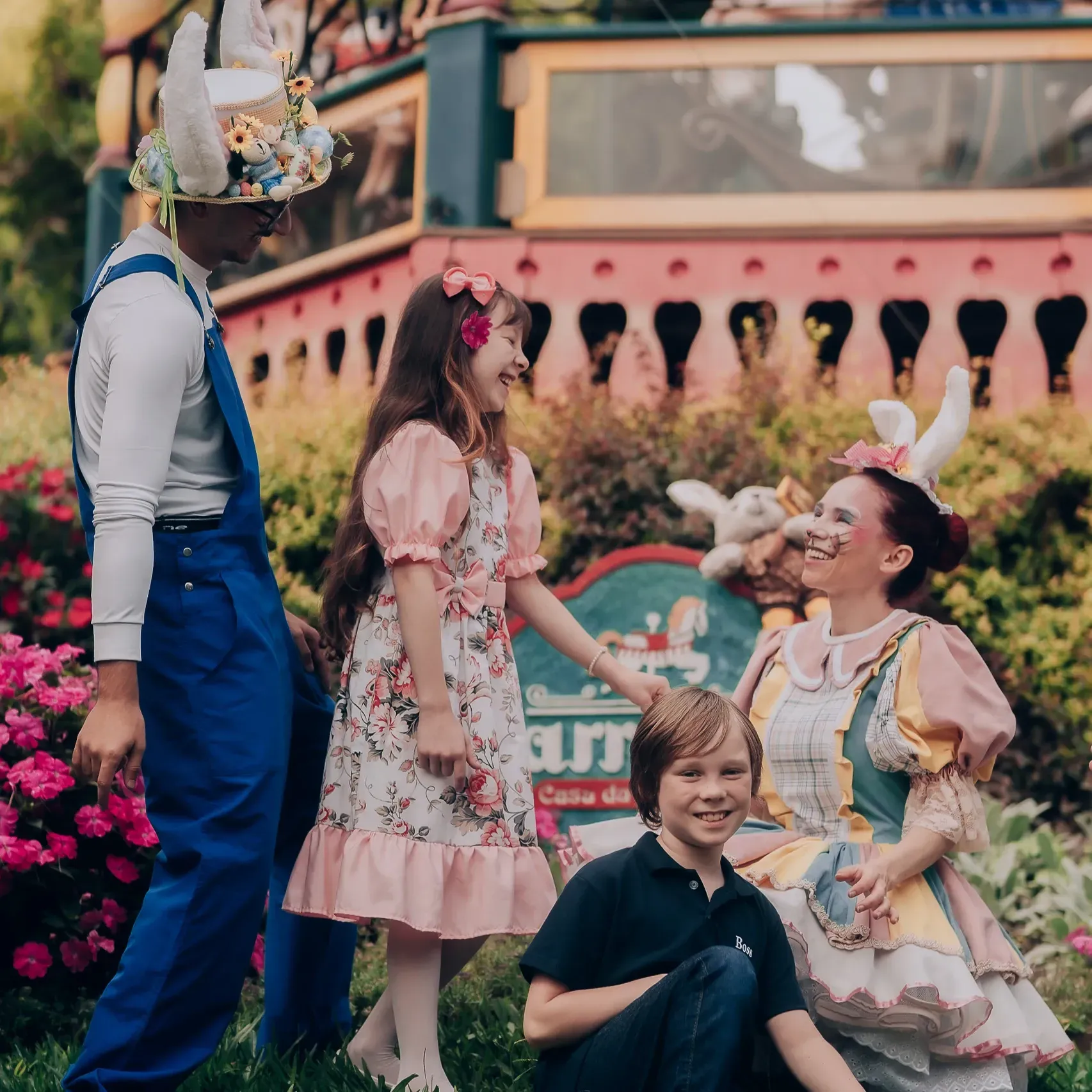Apresentação colorida ao ar livre com artistas fantasiados e crianças posando em um cenário de jardim encantador.