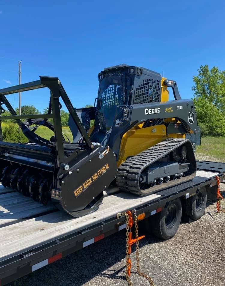 John Deere skid steer with mulching head on a trailer, ready for land clearing.