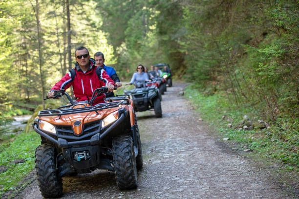 People riding ATVs on a dirt path through a forest.