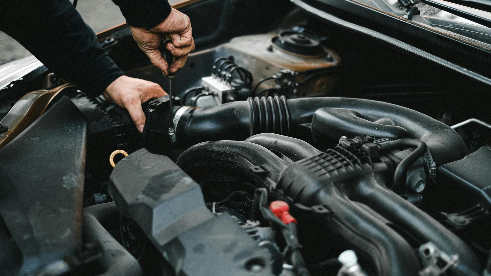 Mechanic working on a car engine, using a screwdriver. Hands and engine are visible.