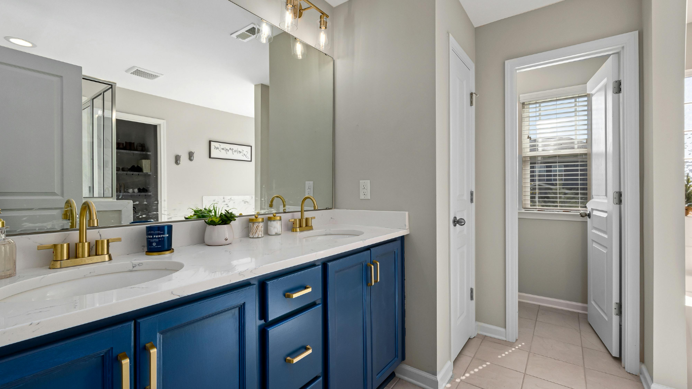 Small bathroom with white fixtures, glass shower, and wooden shelving. Grey tiles and towels.