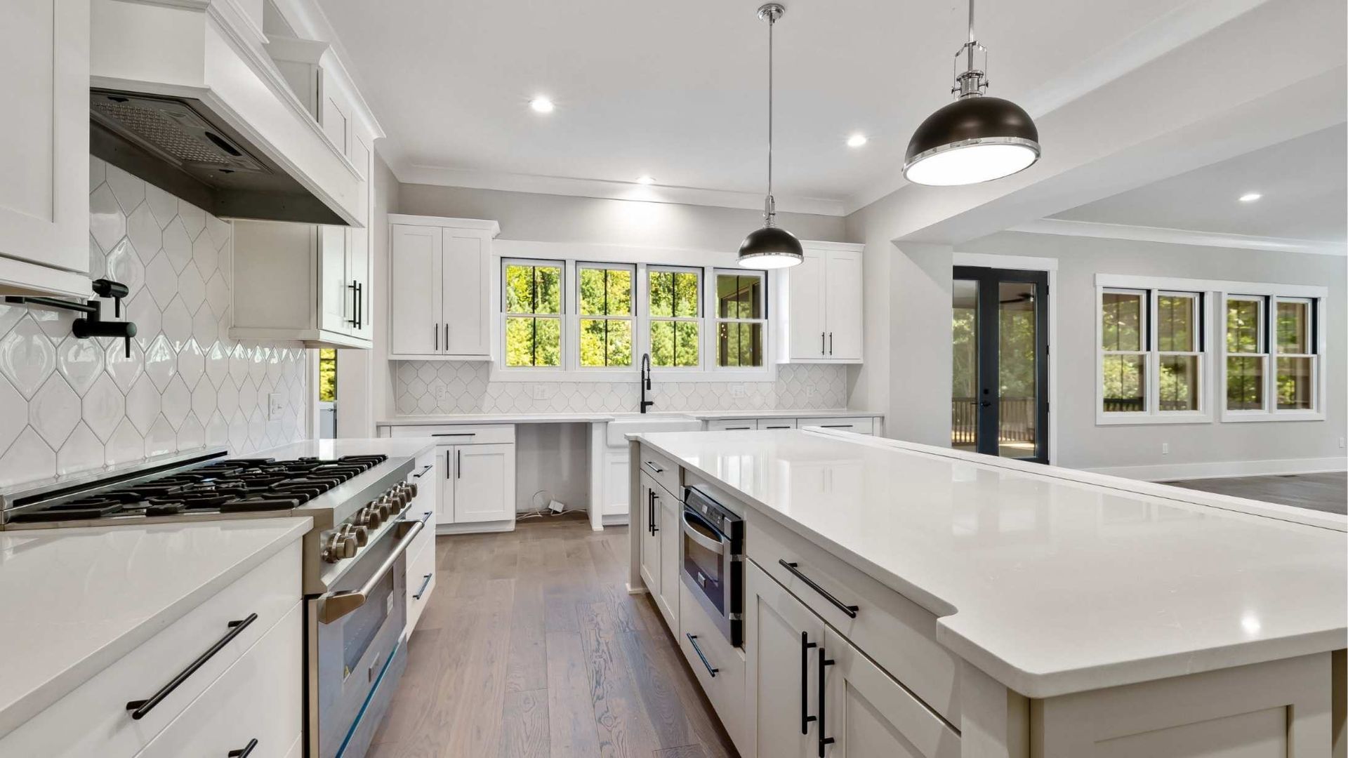 Modern white kitchen with island, stainless steel appliances, and large windows.