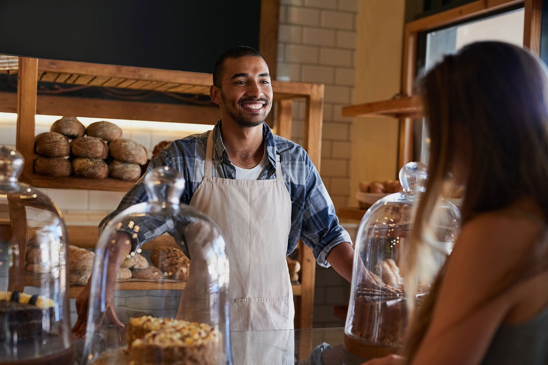 A man is standing behind a counter in a bakery talking to a woman.