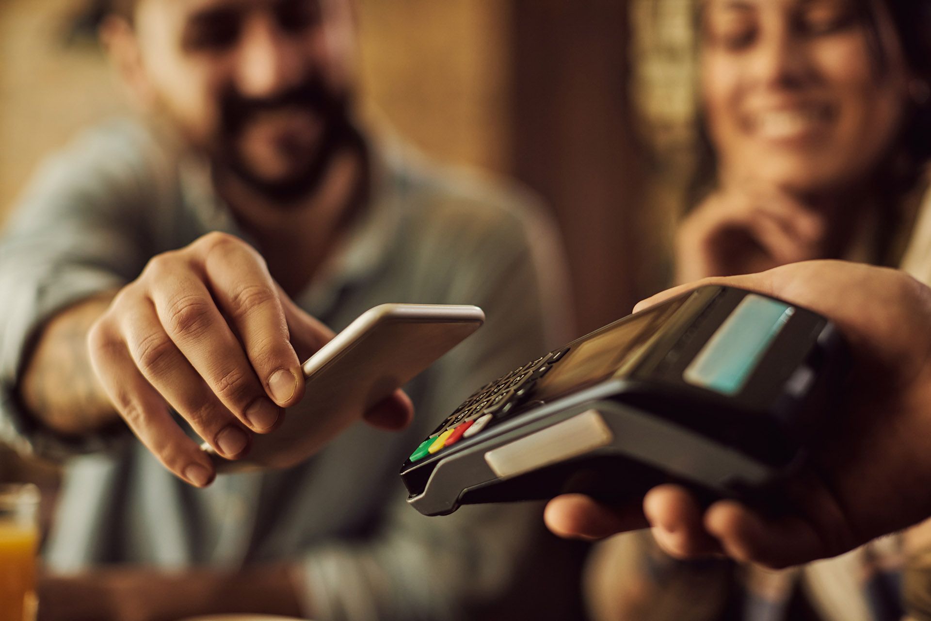A man is using a smart phone to pay a woman with a credit card.