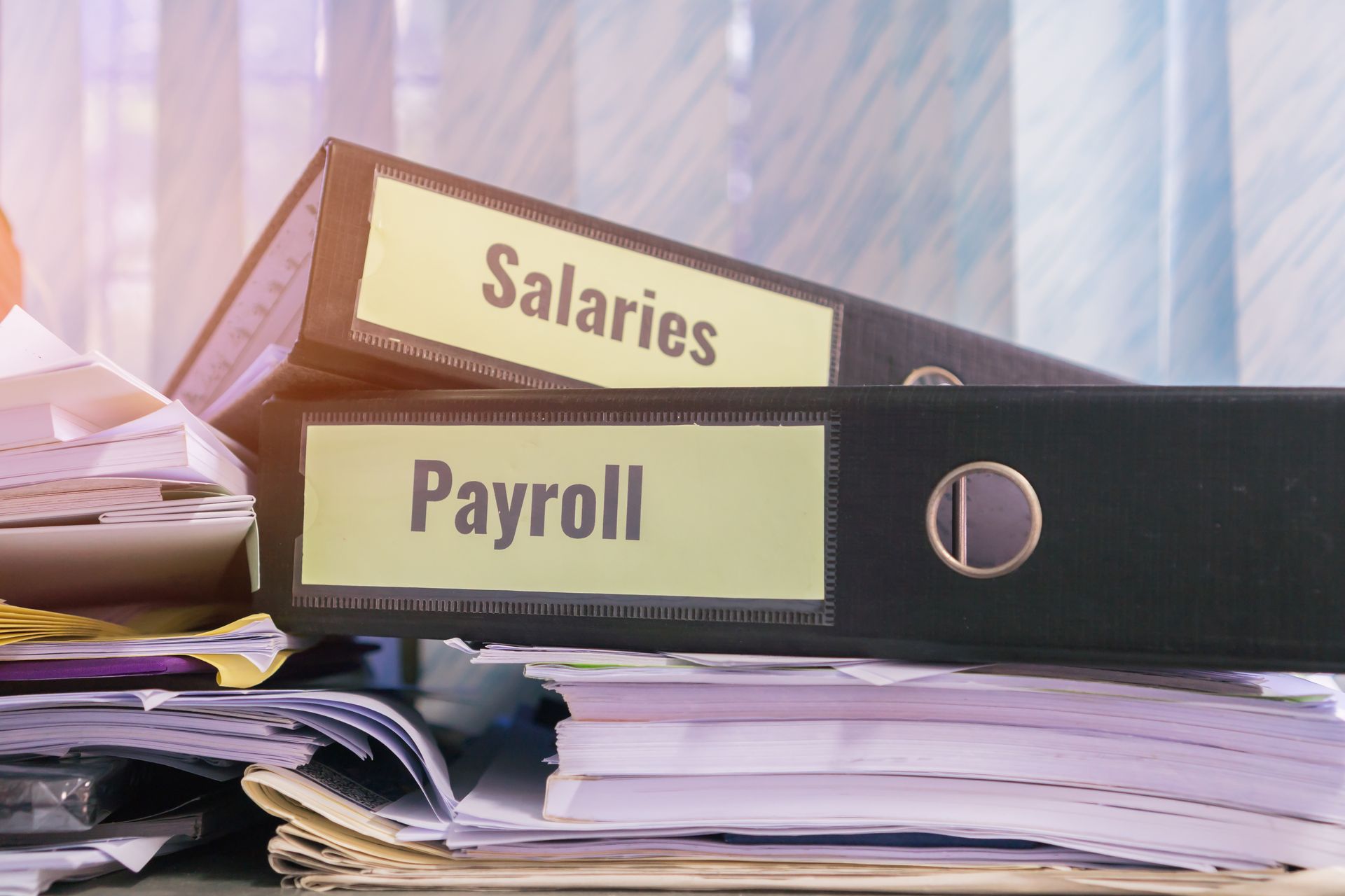 Two binders labeled salaries and payroll are stacked on top of a pile of papers.