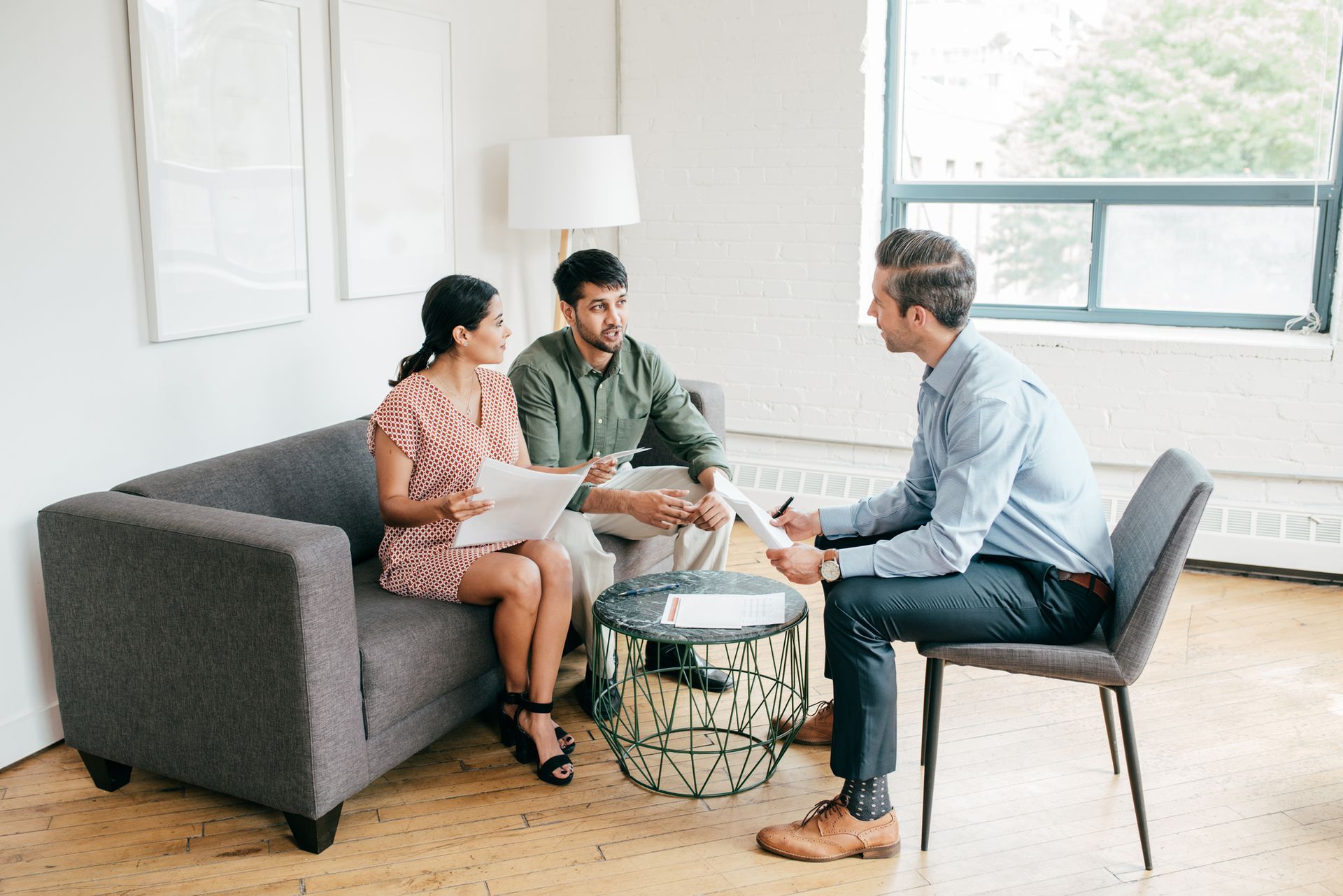 A man is sitting at a table talking to a couple sitting on a couch.