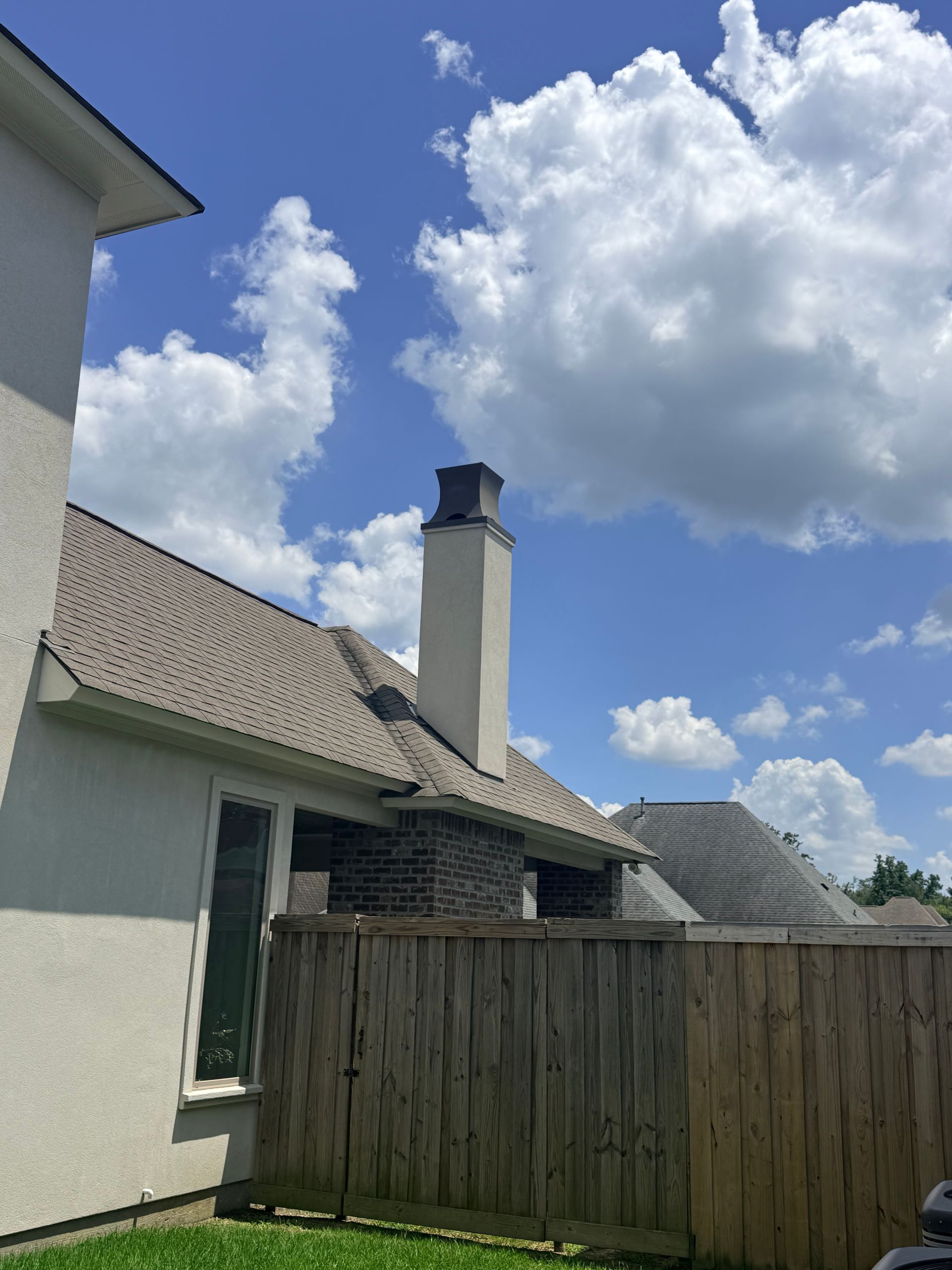 Backyard with white house, wooden fence, and blue sky with large clouds