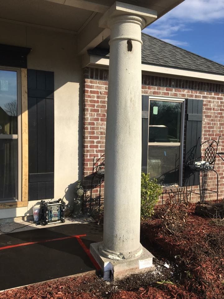 Front porch with a tall stone column, brick wall, glass door, and a wheelbarrow near the entrance.