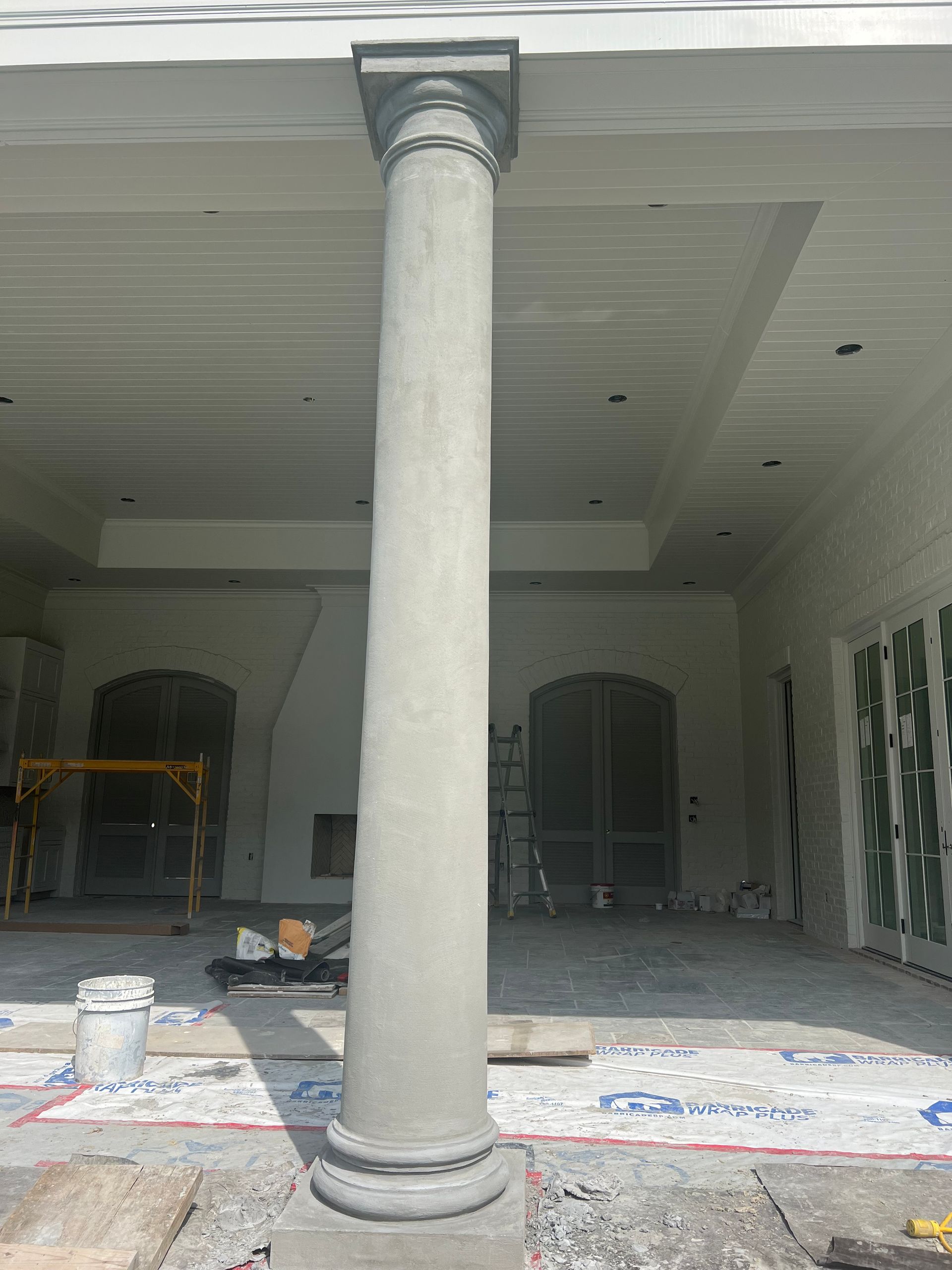 Single concrete column in an unfinished indoor space with drop cloths and construction materials.