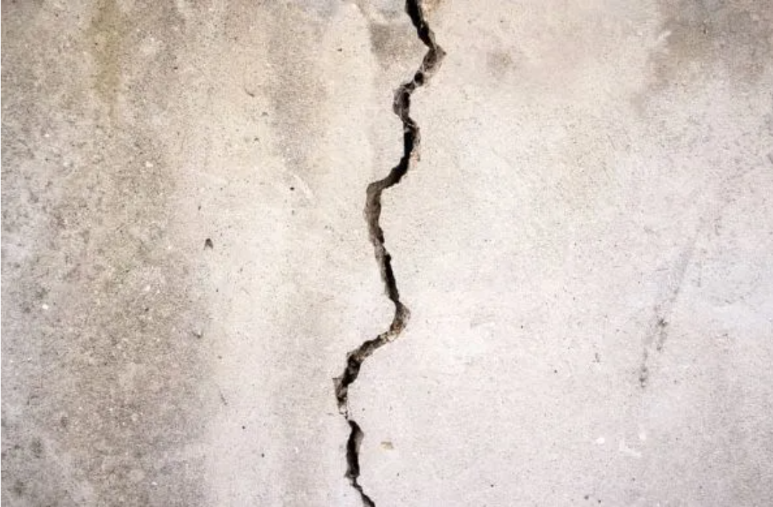 Vertical crack in a light-colored concrete wall or plaster surface.
