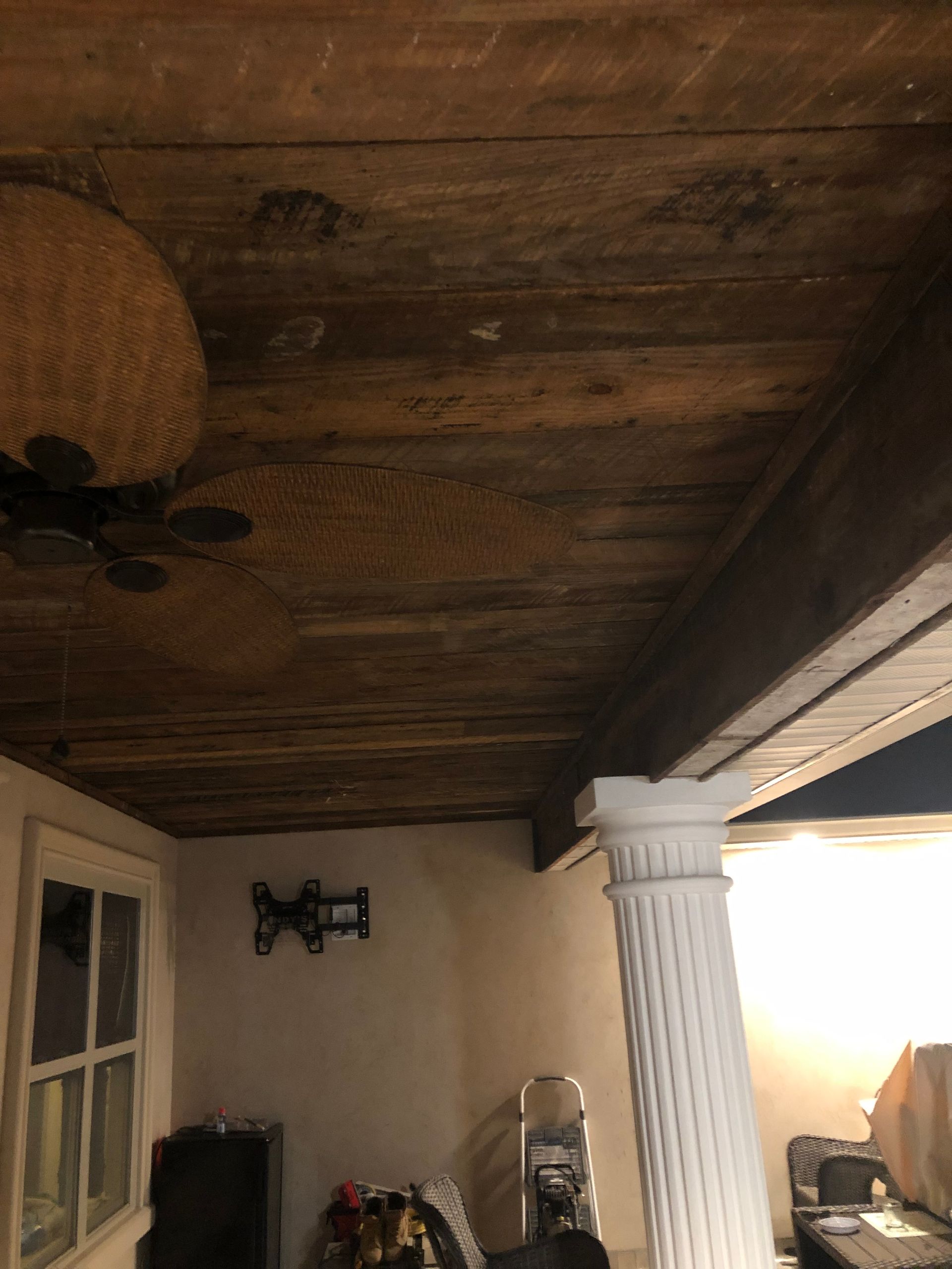 Covered porch with dark wood ceiling, white column, ceiling fan, and bright sunlight at the edge.