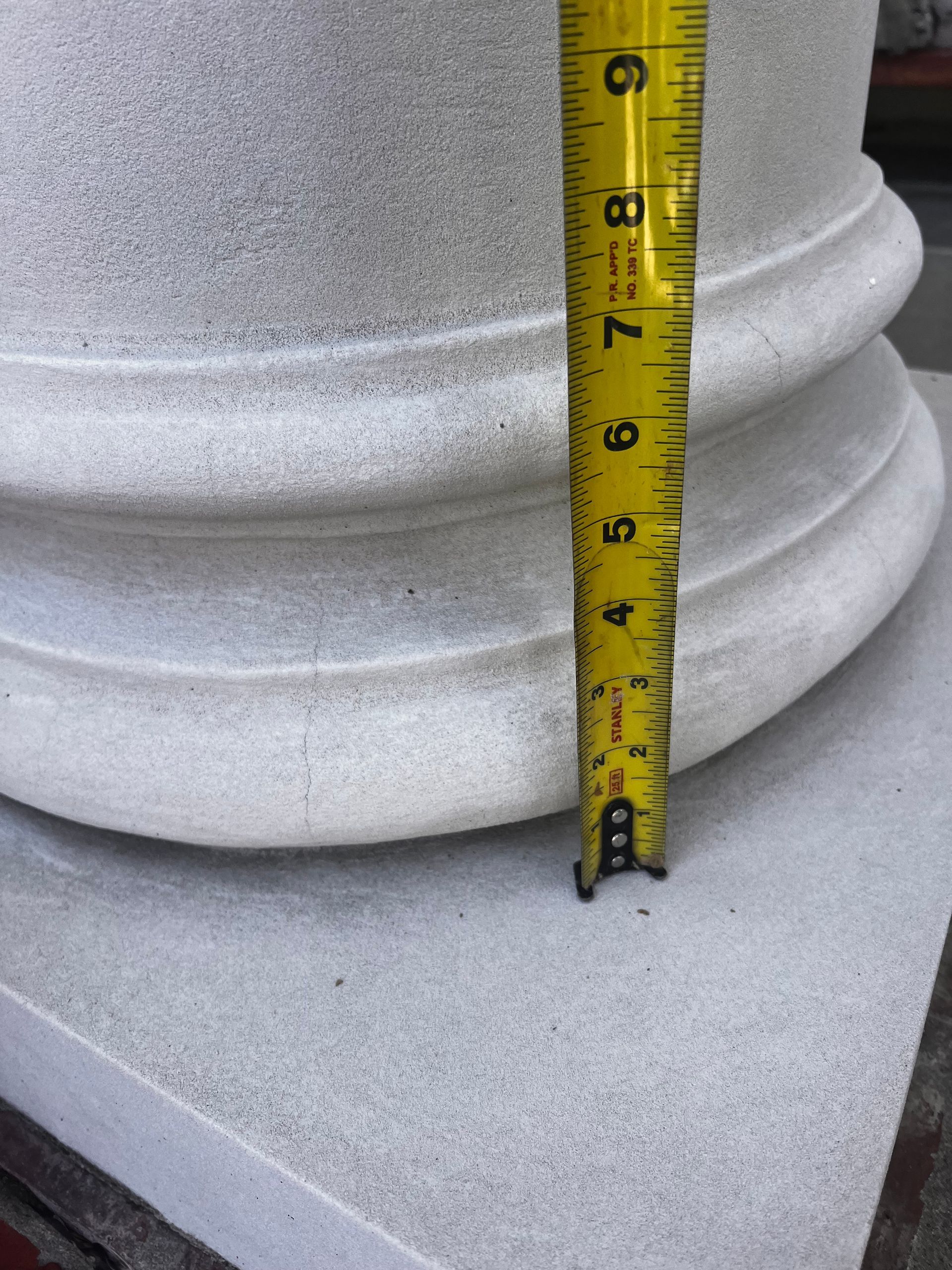 Tape measure against a white column base on a concrete surface