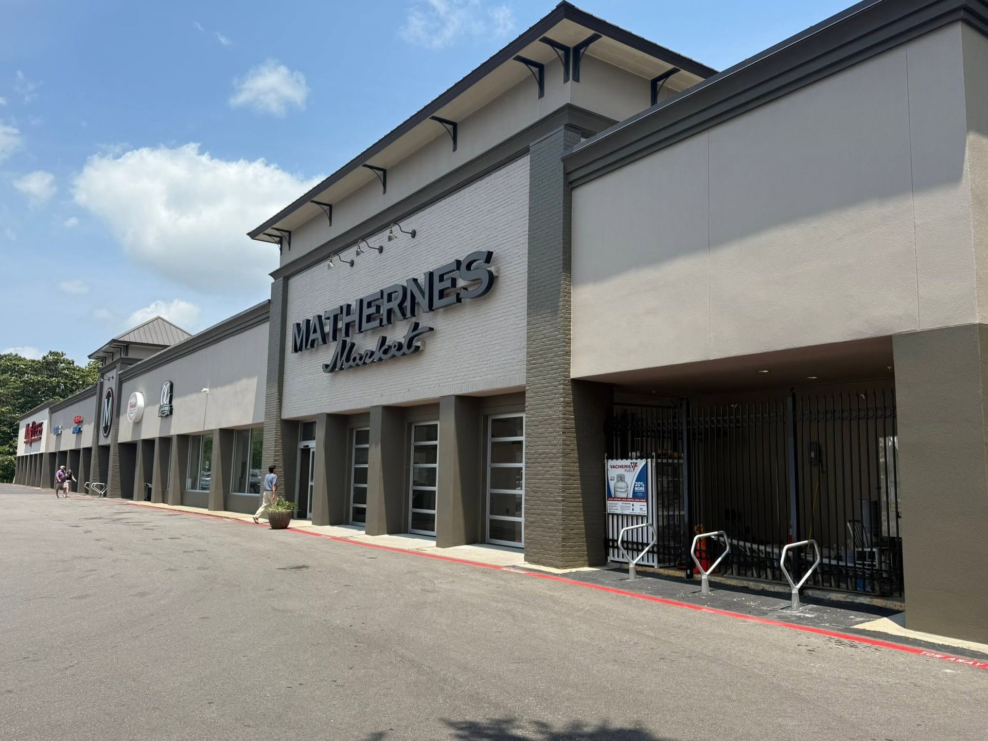 Strip mall storefront with gray facade, large sign, and bike racks along a sunny sidewalk.