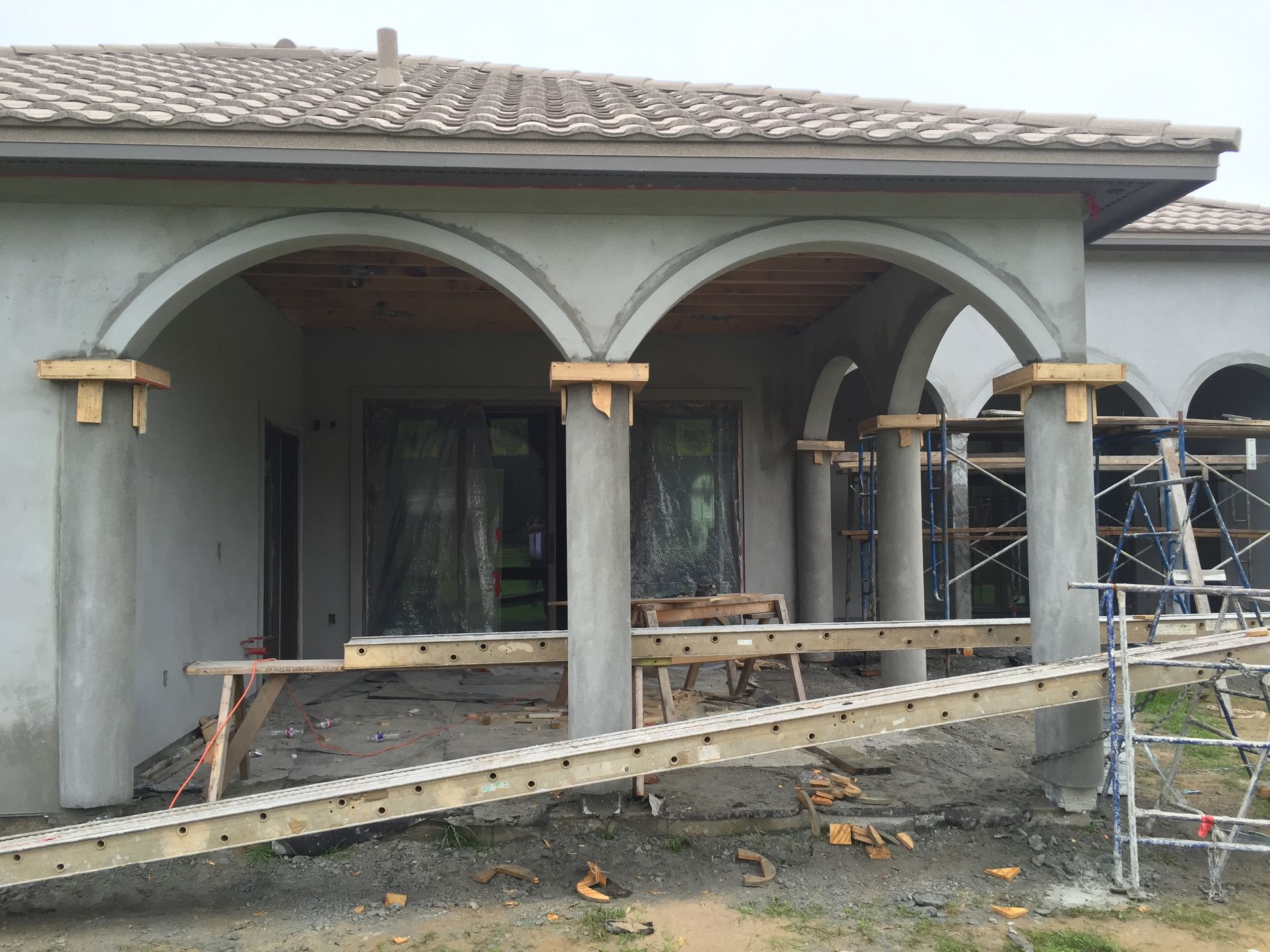 House exterior with arched porch under construction, featuring scaffolding and unfinished stucco.