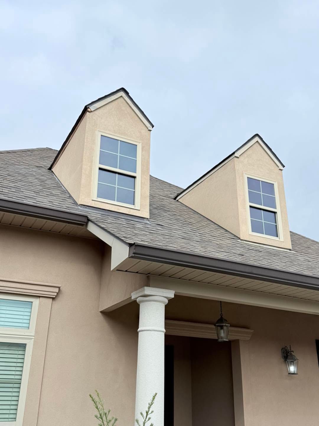Beige house exterior with gray shingle roof and two dormer windows above a front porch