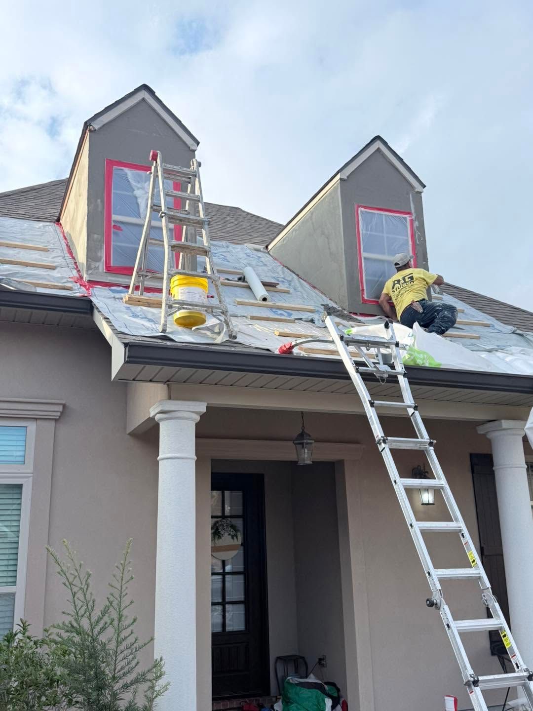 Workers on ladders repairing a roof on a house with dormer windows
