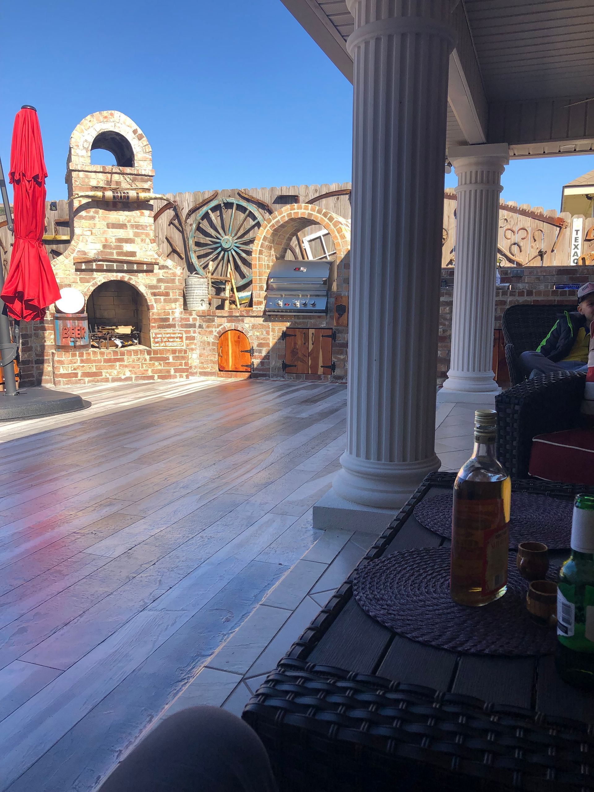 Sunlit stone terrace with arches, a column, and a large wheel-like structure under a clear blue sky