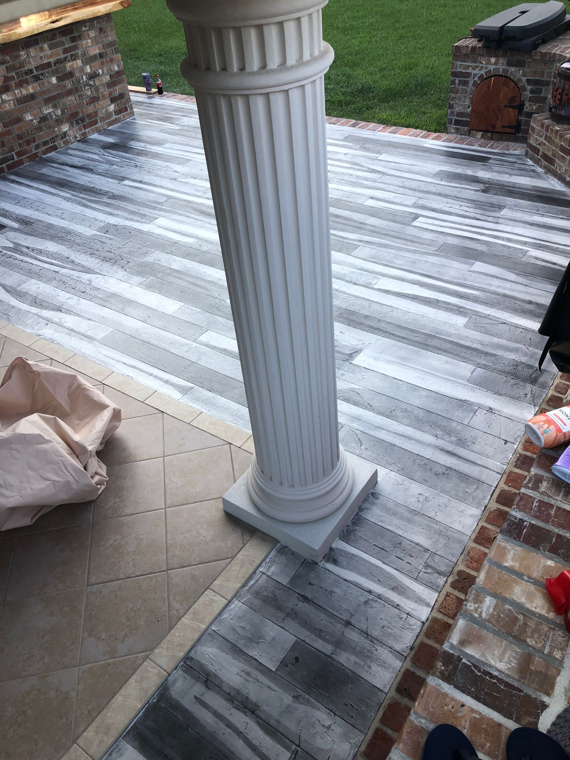White porch column on a gray striped deck beside brick steps and a tan patio floor