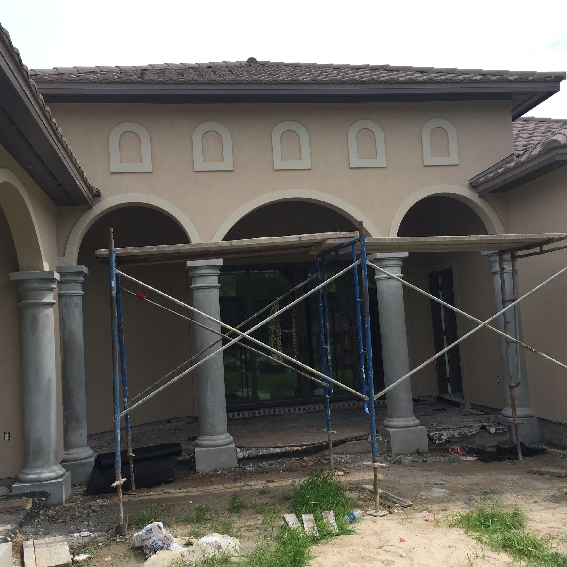 Front view of a stucco house with arched porch, columns, and construction scaffolding in front