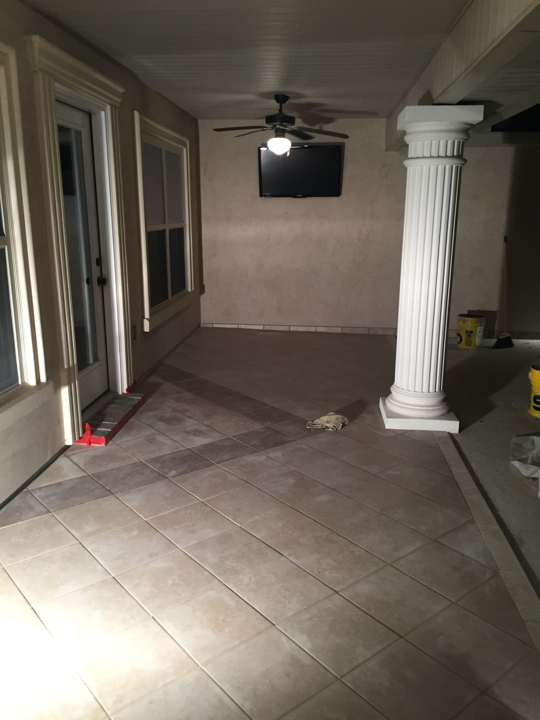Covered patio with tiled floor, white column, ceiling fan, and sliding glass doors at night