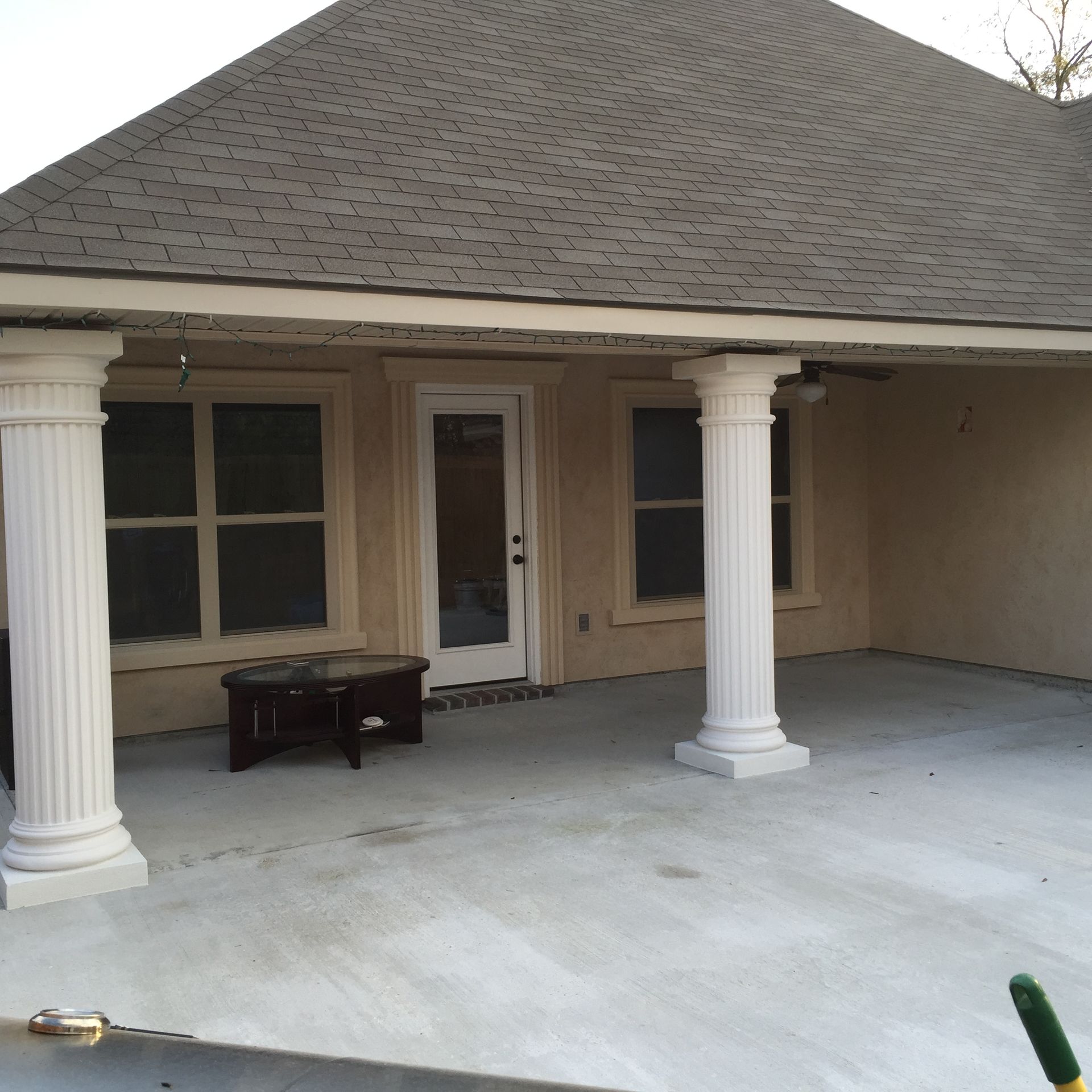 Covered front porch with white columns, beige siding, and a double glass door, with a bench on the concrete floor