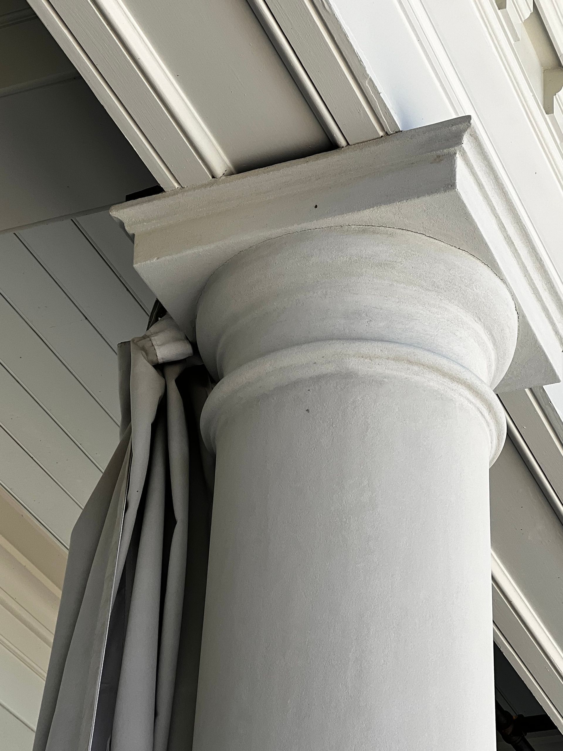 White decorative column under a porch ceiling with light gray trim and siding